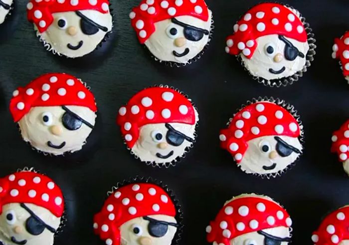 A top-down view of cupcakes designed to resemble pirate faces, complete with fondant kerchiefs and eyepatches adorned with playful polka dots.