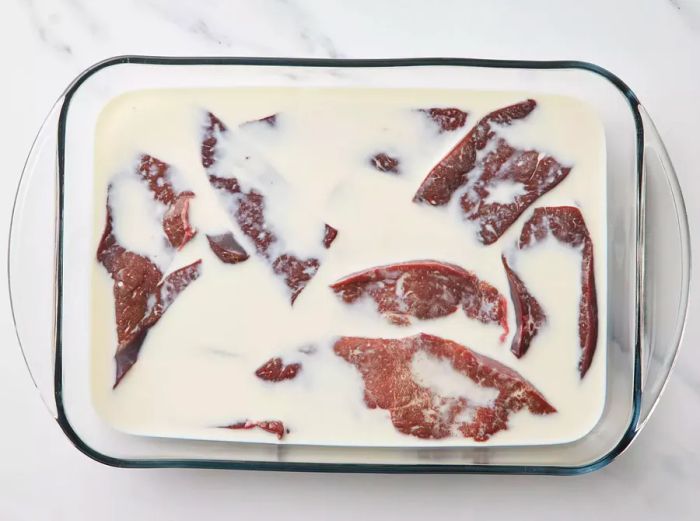 A large baking dish with liver slices soaking in milk