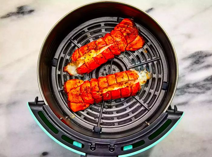 An air fryer basket holding two perfectly cooked lobster tails