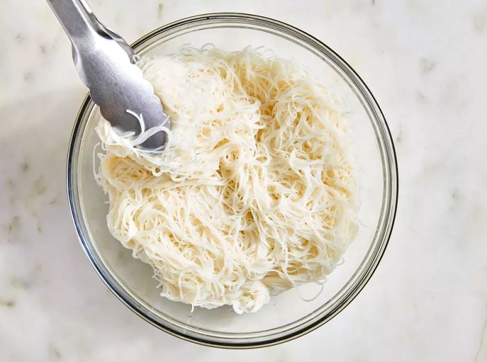 Aerial view of cooked and drained vermicelli noodles in a glass bowl.