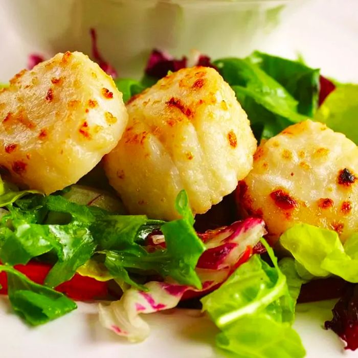 A close-up of broiled scallops served on a bed of salad greens