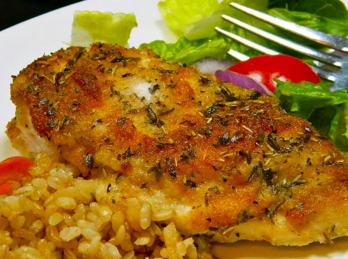 A close-up shot of baked chicken served with brown rice and a fresh salad