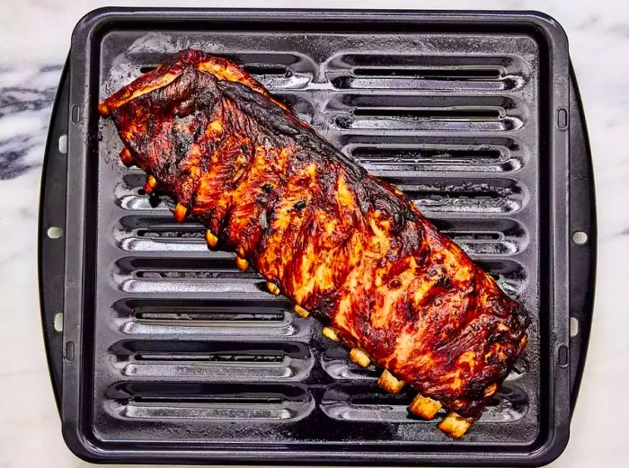 A rack of marinated and cooked Chinese spareribs resting above a broiler tray