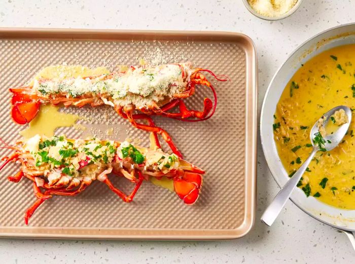 A baking sheet with a lobster halved lengthwise, topped with a buttery sauce and a sprinkle of Parmesan cheese.