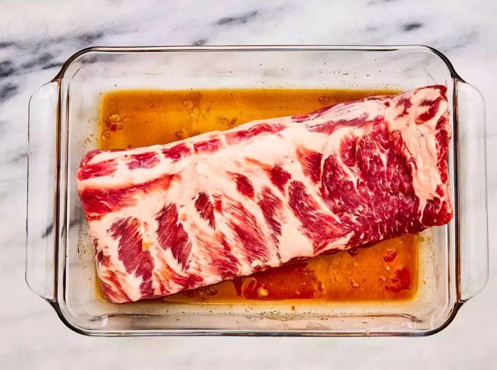 A glass dish containing pork spareribs marinated in a hoisin-soy mixture