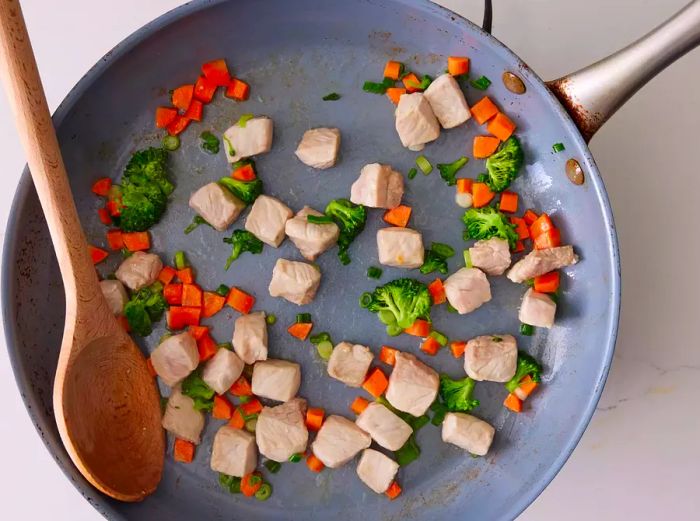 A large skillet filled with cooked pork, carrots, broccoli, and green onions.