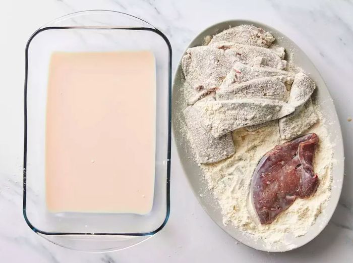 A large plate of flour-coated liver slices next to a baking dish of milk