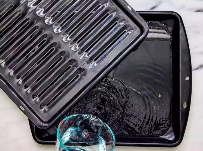 A measuring cup of water being poured into a broiler tray