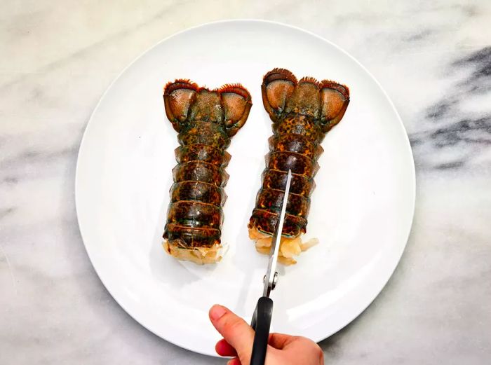 A pair of scissors cutting through the lobster tail's top shell