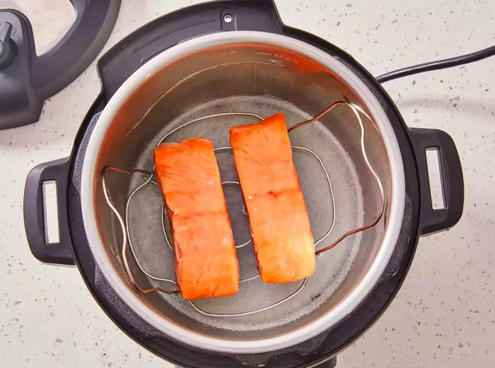 Frozen salmon fillets placed skin-side down on the rack in the pressure cooker.