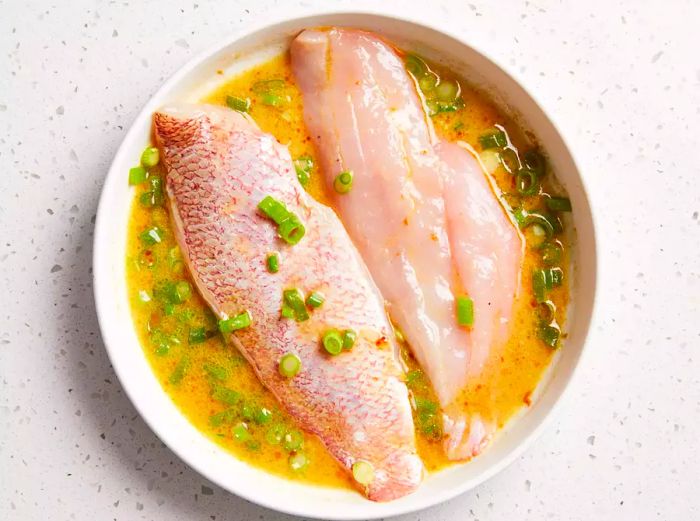 Snapper being dipped in marinade to coat both sides.