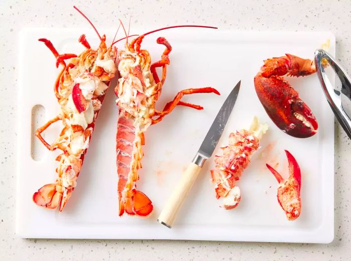 A cutting board displaying a lobster, halved lengthwise, with the meat removed and chopped.