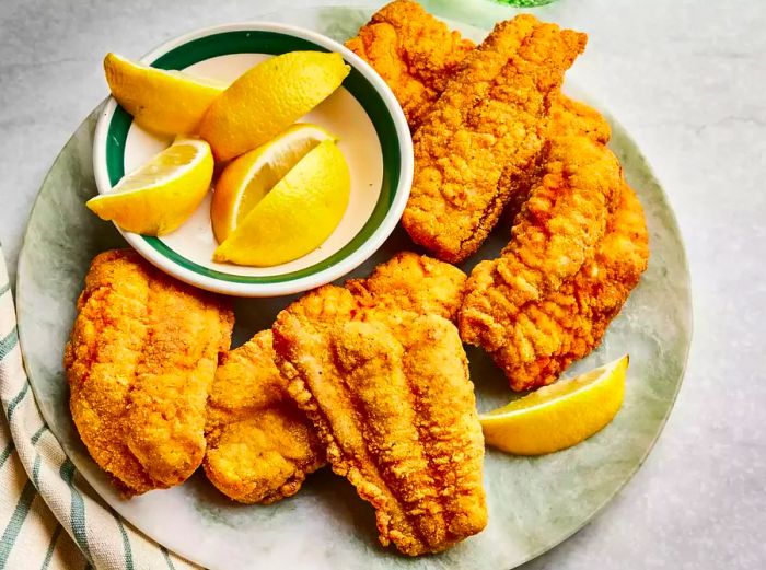 A serving platter of crispy southern-fried catfish, accompanied by fresh lemon wedges.