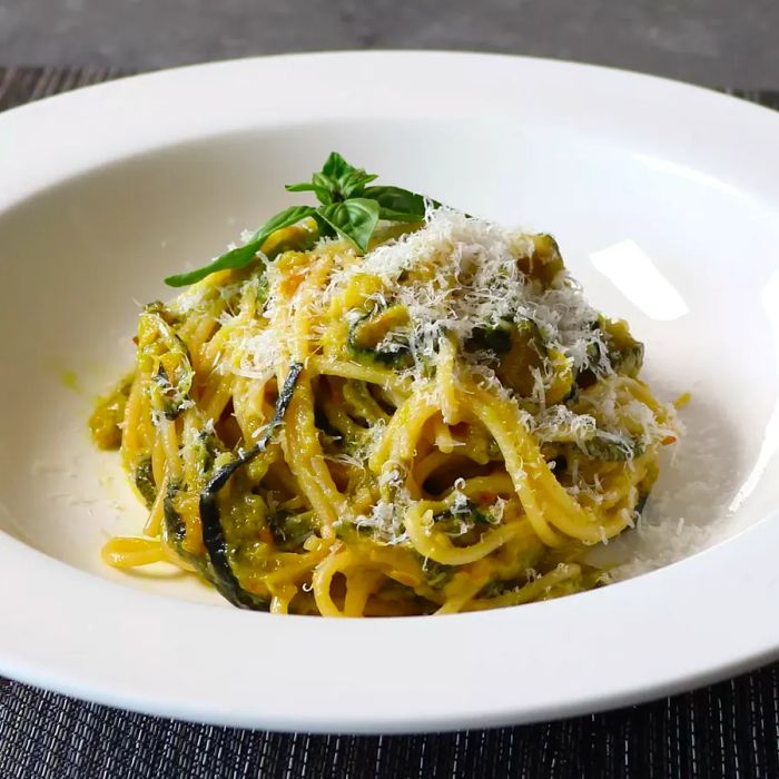 <p> A close-up shot of Zucchini Spaghetti, beautifully garnished with fresh basil and a sprinkle of grated cheese, served in a white bowl.</p>