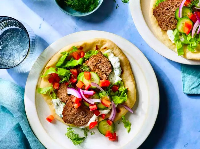 A plate with a pita loaded with gyro meat, fresh vegetables, and creamy yogurt sauce