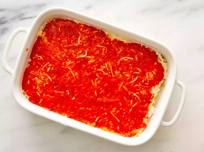 A baking dish with multiple layers of lasagna noodles, filling, and cheese, topped with a layer of tomato sauce