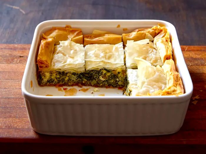 Close-up shot of spanakopita in a baking dish, resting on a wooden cutting board.