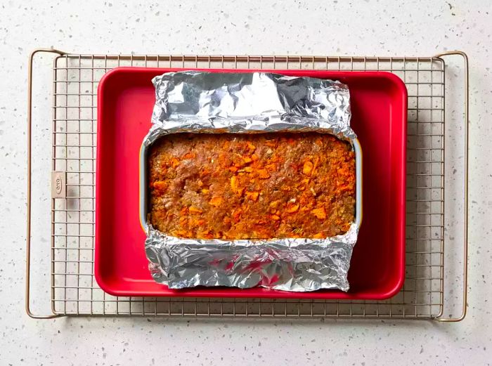 Stovetop Stuffing Meatloaf mixture in a loaf pan lined with aluminum foil, sitting on a baking sheet and cooling rack