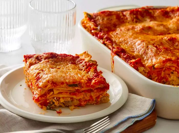 A plated slice of spinach lasagna next to the baking dish containing the rest of the lasagna