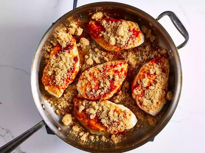 Chicken breasts in a skillet, seasoned with a mix of brown sugar and paprika.