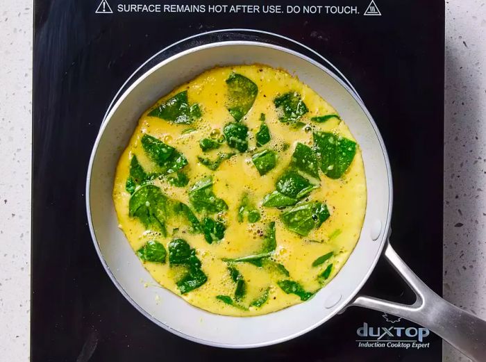 A nonstick skillet holding a raw baby spinach omelet