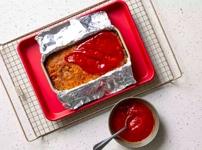 Ketchup glaze spread over the top of the Stovetop Stuffing Meatloaf in a loaf pan, placed on a baking sheet and cooling rack