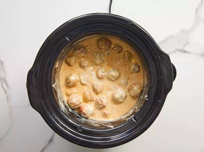 A slow cooker filled with Swedish meatballs in gravy.