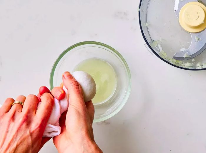 Two hands squeezing the liquid out of a towel filled with processed onion