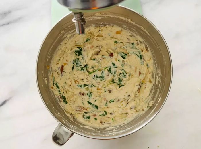 A mixture of ricotta cheese and spinach in the bowl of a stand mixer