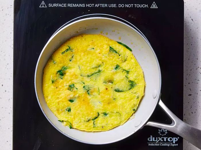 A nonstick skillet with a perfectly cooked baby spinach omelet