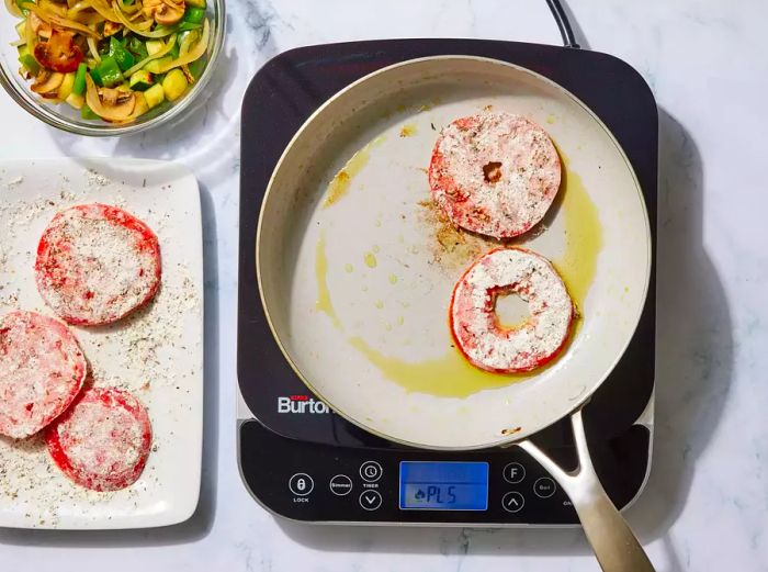 A skillet with tomato slices coated in flour sizzling in oil