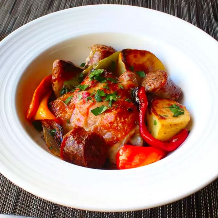 A close-up shot of Chicken, Sausage, Peppers, and Potatoes, topped with fresh herbs, served in a white bowl.