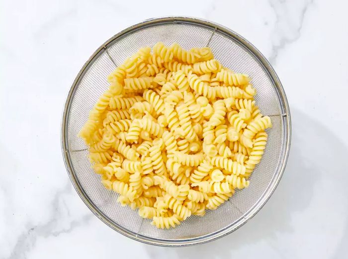 A colander filled with cooked rotini pasta