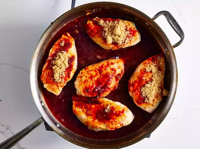 Chicken breasts cooking in a skillet, with red wine poured over them.