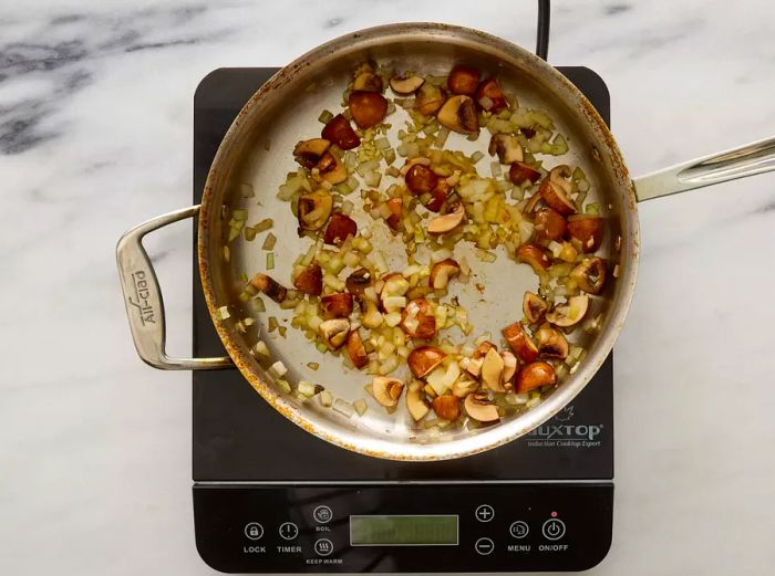 A skillet with mushrooms, onions, and garlic sizzling in olive oil