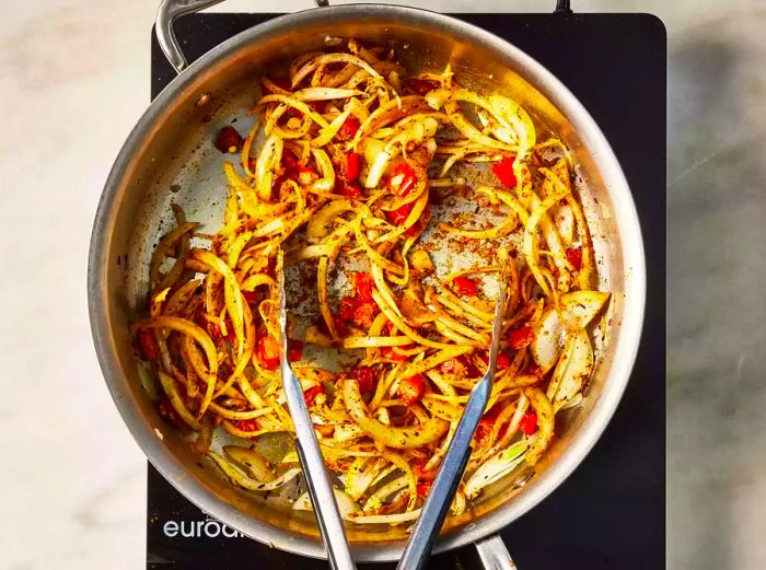 A skillet with onions and tomatoes simmering in spices