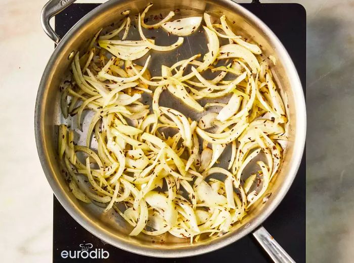 A skillet with cumin seeds, sliced onions, garlic, and ginger