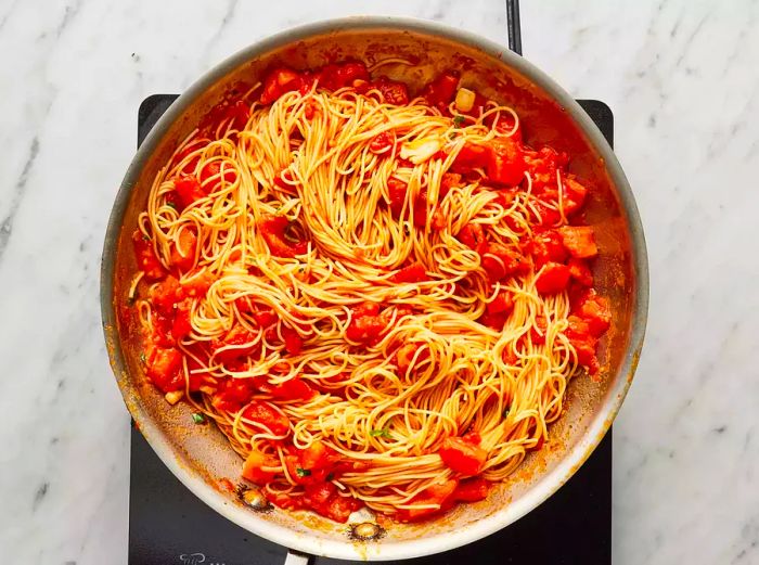 An overhead view of pasta and tomato sauce cooking together in a pan.