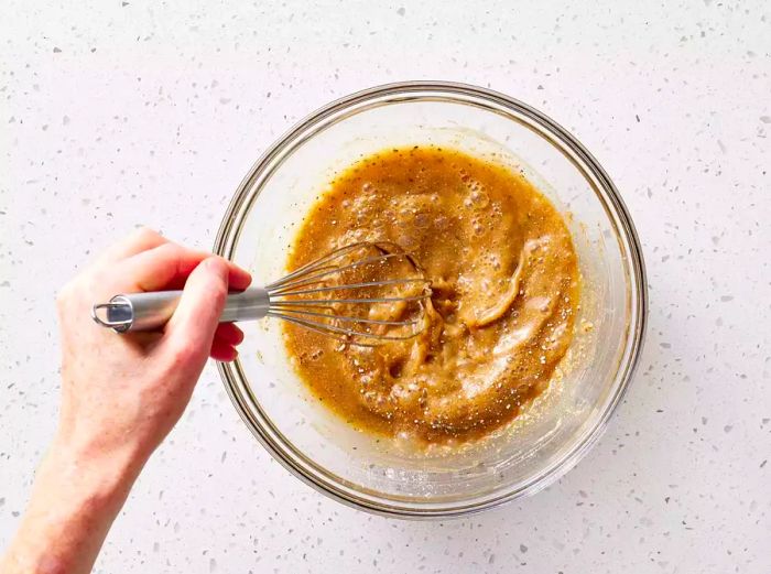 A glass bowl containing ranch seasoning, Italian seasoning, and brown gravy mix being whisked with water.