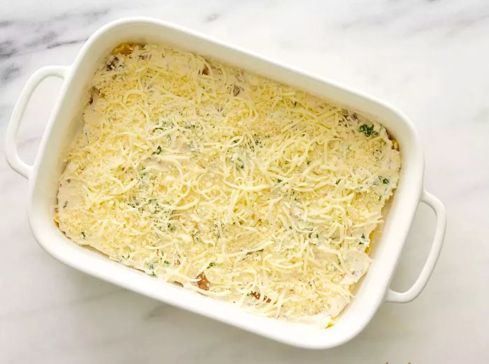 A baking dish filled with layers of lasagna noodles, ricotta-spinach mixture, and shredded cheese