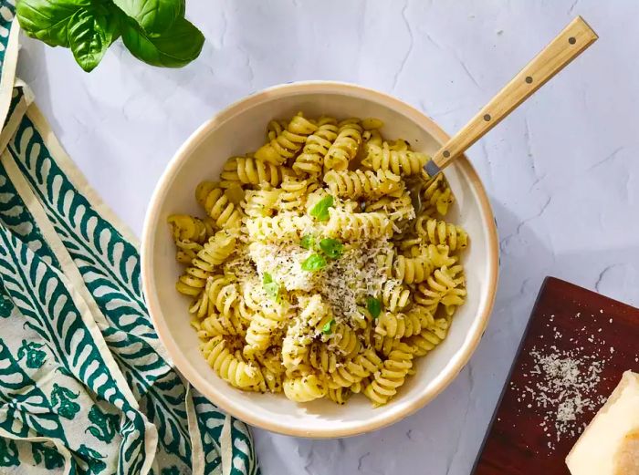 A bowl of pesto pasta, garnished with Parmesan cheese and fresh basil leaves