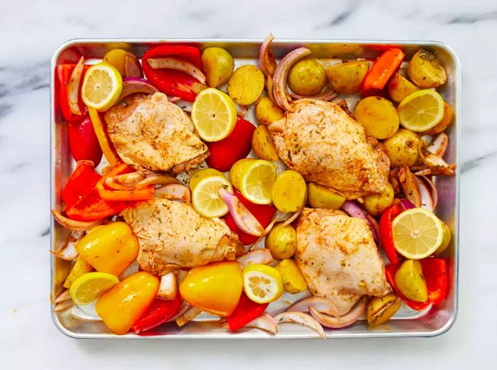 The chicken and vegetable mixture is evenly spread out on the baking sheet.