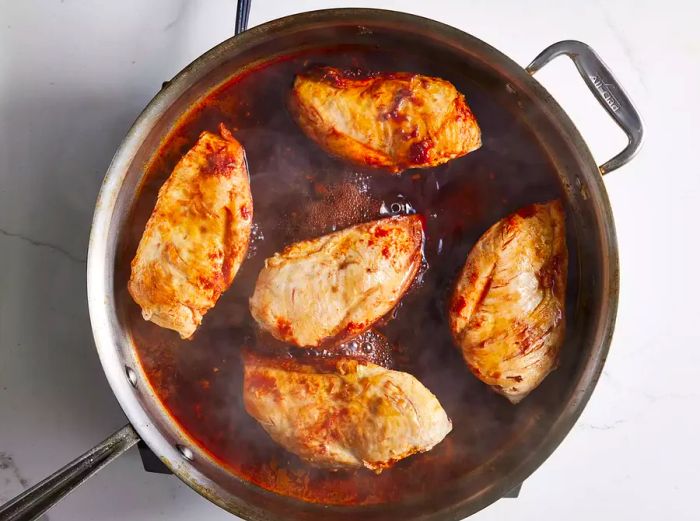 Chicken breasts simmering in red wine in a skillet.