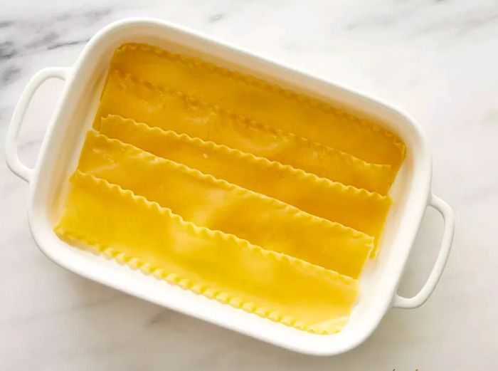 A 13x9-inch baking dish with five cooked lasagna noodles laid out inside