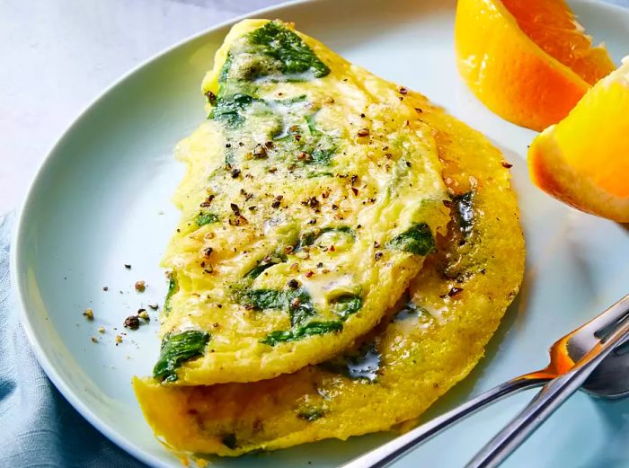 A baby spinach omelet plated with slices of fresh orange