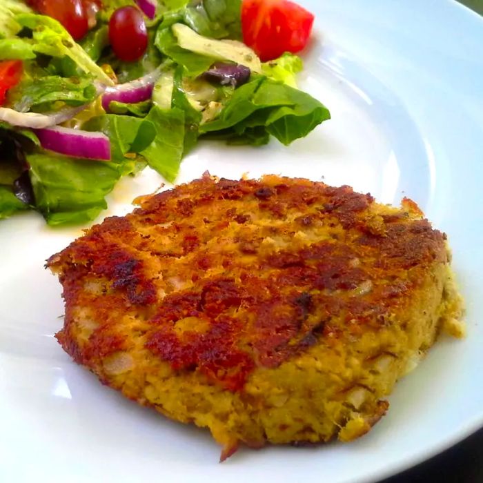 A close-up shot of a Spicy Tuna Fish Cake served with a fresh salad on a white plate.