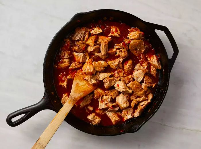 A top-down view of water and tamarind soup base being stirred and cooked with pieces of pork.