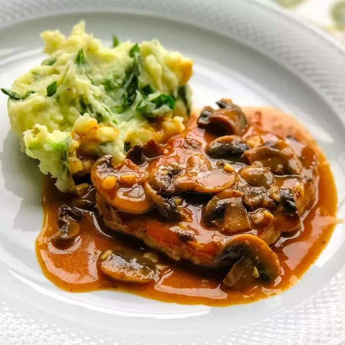 Close-up shot of Pork Chops in Garlic Mushroom Sauce paired with mashed potatoes on a white plate.