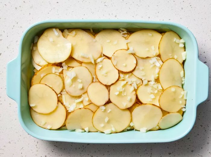 A baking dish filled with layers of sliced potatoes, topped with chopped onions.