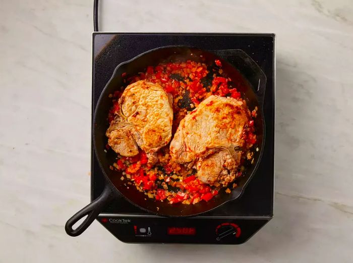 Top-down view of two pork chops cooking over chopped vegetables in a skillet.